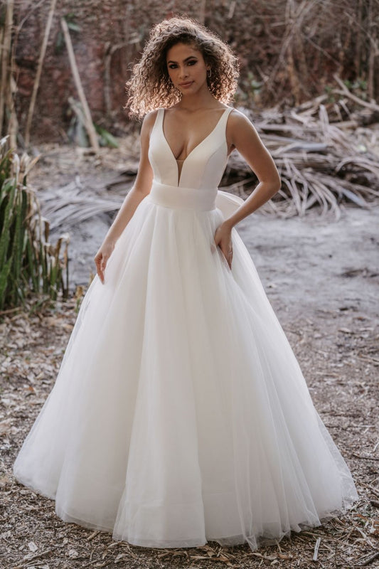 Classic ball gown wedding dress with a deep V-neckline and a voluminous tulle skirt, perfect for a bride seeking a timeless yet modern look for a romantic outdoor or destination wedding.