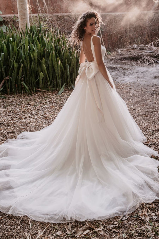 Classic ball gown wedding dress with a deep V-neckline and a voluminous tulle skirt, perfect for a bride seeking a timeless yet modern look for a romantic outdoor or destination wedding.