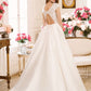 A bride is shown from the back, highlighting a wedding gown with a stunning lace bodice and an open keyhole back. The dress features a full satin skirt that flows into a sweeping train, creating a dramatic and elegant silhouette. The floral-decorated room enhances the romantic ambiance of the scene.