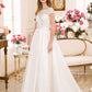 A bride wearing a classic A-line wedding gown with a lace bodice and cap sleeves. The gown features a high neckline and a full satin skirt that gracefully flows to the floor, creating an elegant and timeless look. The scene is set in a bright, floral-decorated room, enhancing the gown's romantic charm.
